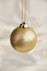 Gold Christmas Ornament on Soft White Fabric. Christmas decoration featuring a glittering golden bauble resting on a smooth white fabric background with soft, warm fairy lights, minimalism and winter-