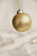Gold Christmas Ornament on Soft White Fabric. Christmas decoration featuring a glittering golden bauble resting on a smooth white fabric background with soft, warm fairy lights, minimalism and winter-