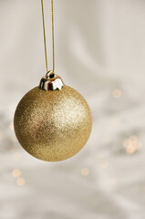 Gold Christmas Ornament on Soft White Fabric. Christmas decoration featuring a glittering golden bauble resting on a smooth white fabric background with soft, warm fairy lights, minimalism and winter-