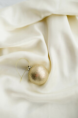 Gold Christmas Ornament on Soft White Fabric. Christmas decoration featuring a glittering golden bauble resting on a smooth white fabric background with soft, warm fairy lights, minimalism and winter-
