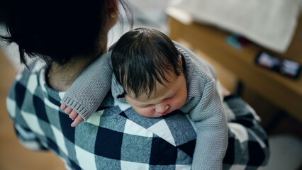 Mother gently cradling her newborn baby on her shoulder in a serene, sunlit room. The baby is peacefully sleeping, highlighting the love and tenderness in their bond