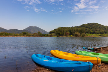 Colorful kayaks resting by a tranquil lake, surrounded by green hills and a clear blue sky, perfect for outdoor adventure and relaxation.