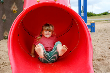 Little preschool girl playing on outdoor playground. Happy toddler child climbing and having fun...