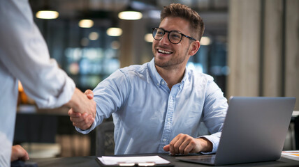 A happy young candidate man and HR manager handshaking in a job interview in office. Business career, hiring, recruiting new employee or placement, greeting, signing contracts, client deal concepts.	