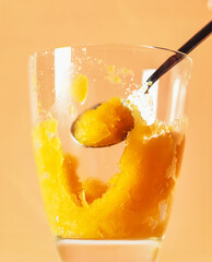 Refreshing Mango Sorbet Served In A Clear Glass With A Spoon. A bright yellow mango sorbet is scooped from a glass, illuminated against a warm orange background