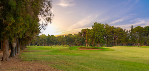 A serene golf course lined with tall trees, illuminated by the soft glow of an evening sky, offering a tranquil outdoor escape.
