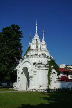 A whitewashed temple with intricate carvings with backdrop of lush greenery and a clear blue sky. Thai temple, Buddhist temple, Wat Suan Dok, Chiang Mai, Thailand