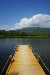 A wooden pier stretches out into a serene lake, offering a peaceful view of the surrounding mountains and clear blue sky