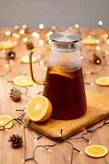 A teapot with mulled wine stands on a table with oranges and a garland