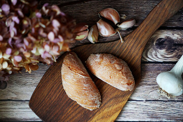 Rustic bread rolls on a wooden board with garlic cloves and dried flowers in the background. Cozy, farmhouse-style composition perfect for food or rustic-themed visuals.