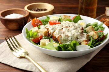Tasty Caesar salad with chicken and tomatoes in bowl served on wooden table, closeup