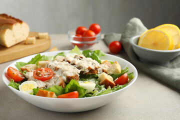 Tasty Caesar salad with chicken and tomatoes in bowl on gray textured table