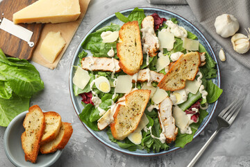 Tasty Caesar salad with chicken, ingredients and fork on gray textured table, flat lay