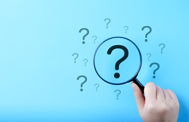 Question Mark and Root Cause Analysis Concept. A hand holding a magnifying glass over a large...