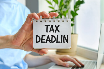 Paper sheet with text TAX DEADLINE in hand, calculator and pencils on wooden table