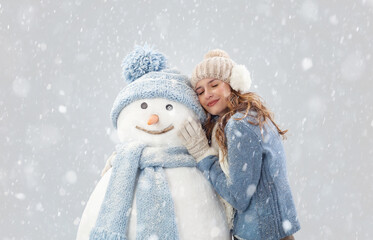 Happy young woman enjoying embracing a snowman in a winter snowfall, dressed in warm winter clothing. Ski trip during the Christmas holidays in winter season. Cooling and Heating temperatures Concept