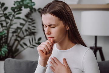 Fototapeta premium Ill upset young caucasian woman sitting on couch freezing blowing running nose got fever cough cold sneezing, sick female having influenza symptoms coughing at home, flu concept