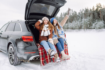 Two young women near a car on a snowy road.  Traveling in Winter.