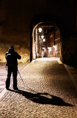 man with tripod photographing night illuminated street with historic houses in old town Klodzko, Poland