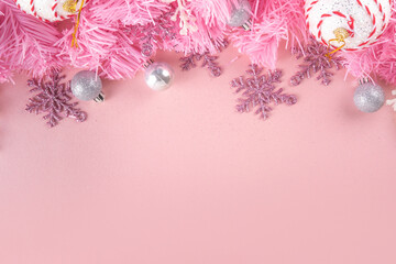 Kitschmas Christmas background with fluffy pink artificial Christmas tree brunches, pink festive bow and decorations in trendy embracing kitsch style, top view flat lay copy space