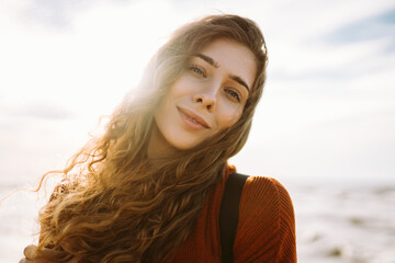 Portrait of woman enjoying a breezy day near a vibrant red lighthouse at sunset. Travel, weekend, relax and lifestyle concept.