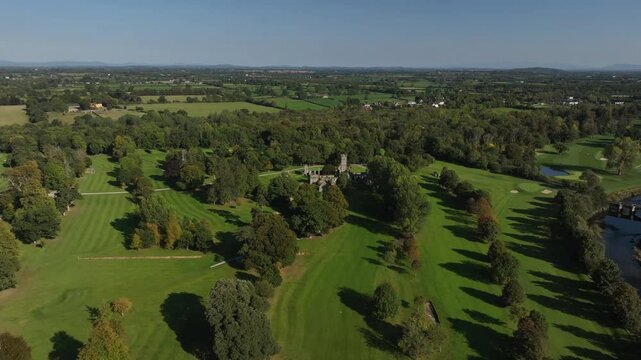 Franciscan Friary, Adare, County Limerick, Ireland, September 2024. Drone orbits clockwise in a panoramic vista of the 15th century ruins among scattered trees with the River Maigue in the distance.