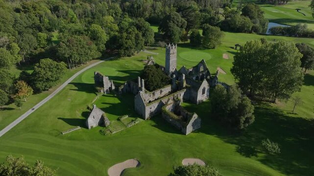 Franciscan Friary, Adare, County Limerick, Ireland, September 2024. Drone orbits counter clockwise and ascends above the ruined building with grassy overgrowth in middle of a scenic golf course.