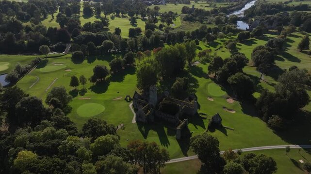 Franciscan Friary, Adare, County Limerick, Ireland, September 2024. Drone orbits clockwise at a high angle from the dark shadow side of ruins to illuminated side as a bird soars in sky on sunny day.