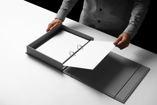 A person handling an A4 mockup sheet from an open, elegantly designed binder box. Isolated blank mockup surface to place your design. 