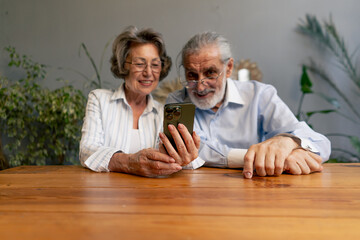 elderly people sitting at a table together watching social networks on the phone funny videos happy old age elderly couple pleasant memories leisure time in old age warm feelings support in old age