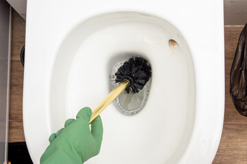 Woman or man in green rubber gloves cleans toilet bowl with toilet brush. Toilet brush with gold handle