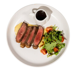 A gourmet dish featuring succulent steak slices, creamy puree, fresh salad, and a rich sauce served...