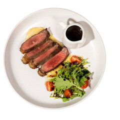 A beautifully plated dish featuring sliced steak on a bed of mashed potatoes, accompanied by a fresh salad and a small serving of sauce.