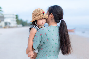 Obraz premium Mother carries her daughter on the beach,Asian mother was carrying her daughter on the beach. little girl sleeps in her mother's arms.