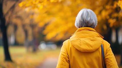 Fototapeta premium A person in a yellow coat walks through a park with autumn foliage.