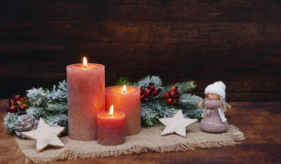 Rustikale Advents und Weihnachtsdekoration mit Kerzen, Zweigen und Weihnachtsschmuck vor einer Holzwand mit Platz für Text.