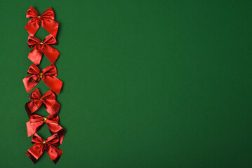 Red bright festive bows on a green background. Christmas decorations. Copy space, flat lay