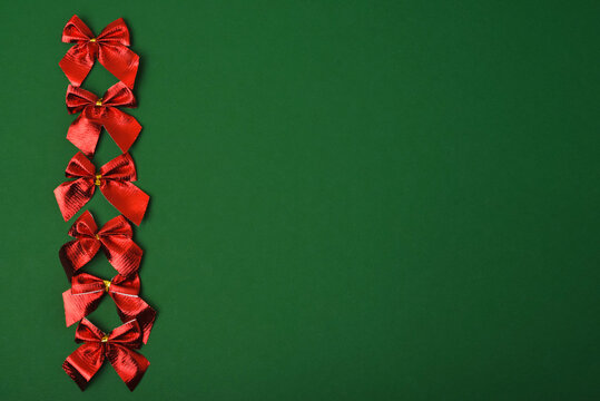 Red bright festive bows on a green background. Christmas decorations. Copy space, flat lay