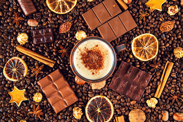 Cup of cappuccino on the background of coffee beans, chocolate pieces, cinnamon, dried orange and star anise.