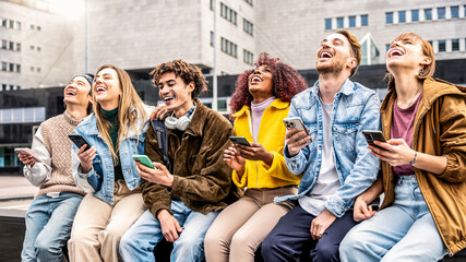 Group of young people using smart mobile phone sitting outdoors - Happy friends with smartphone laughing together watching funny video on social media platform - Tech and modern students concept