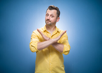 Limit. Man gesturing stop or x sign with her arms, refuses or reject something, guy crossing her hands over blue background, dresses in yellow shirt