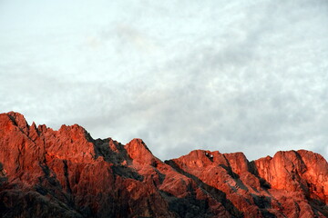 Rot leuchtende Bergkette mit wolkigem Himmel im Hintergrund (Alpenglühen)