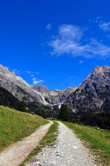 Naklejka premium Schotterweg verläuft ins Bild und verliert sich in der Ferne. Berge und blauer Himmel im Hintergrund