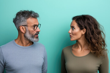 Fototapeta premium Portrait of a happy couple sitting and talking other on turquoise background