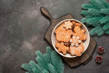 Christmas gingerbread cookies in bowl on wooden cutting board decorated with fir branches, dark grunge background, top view, flat lay, copy space
