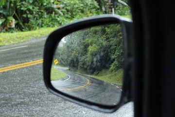 carro em estrada sinuosa em dia de chuva - foto a partir do retrovisor 