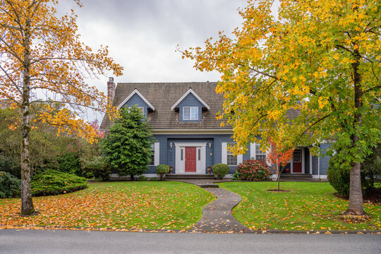 Two story stucco luxury house with garage door, big tree and nice Fall foliage landscape in Vancouver, Canada, North America. Day time on November 2024.