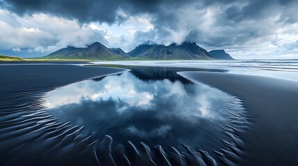 Fototapeta premium A detailed shot of tidal pools on black sand reflecting dramatic storm clouds above