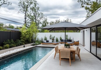 Obraz premium Modern outdoor patio featuring a serene swimming pool, stylish lounge area, and elegant dining set shaded by a large umbrella in a tranquil garden setting.