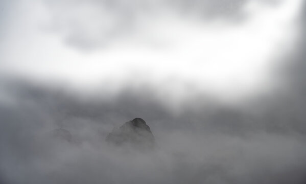 A rocky mountain peak jutting out of the mist and clouds with transparent areas
 - Powered by Adobe